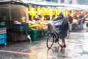 fahrradfahrer-schiebt-fahrrad-in-stroemenden-regen-ueber-einen-wochenmarkt