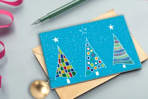 weihnachtskarte-mit-bunten-tannen-daneben-stift-und-weihnachtskugel